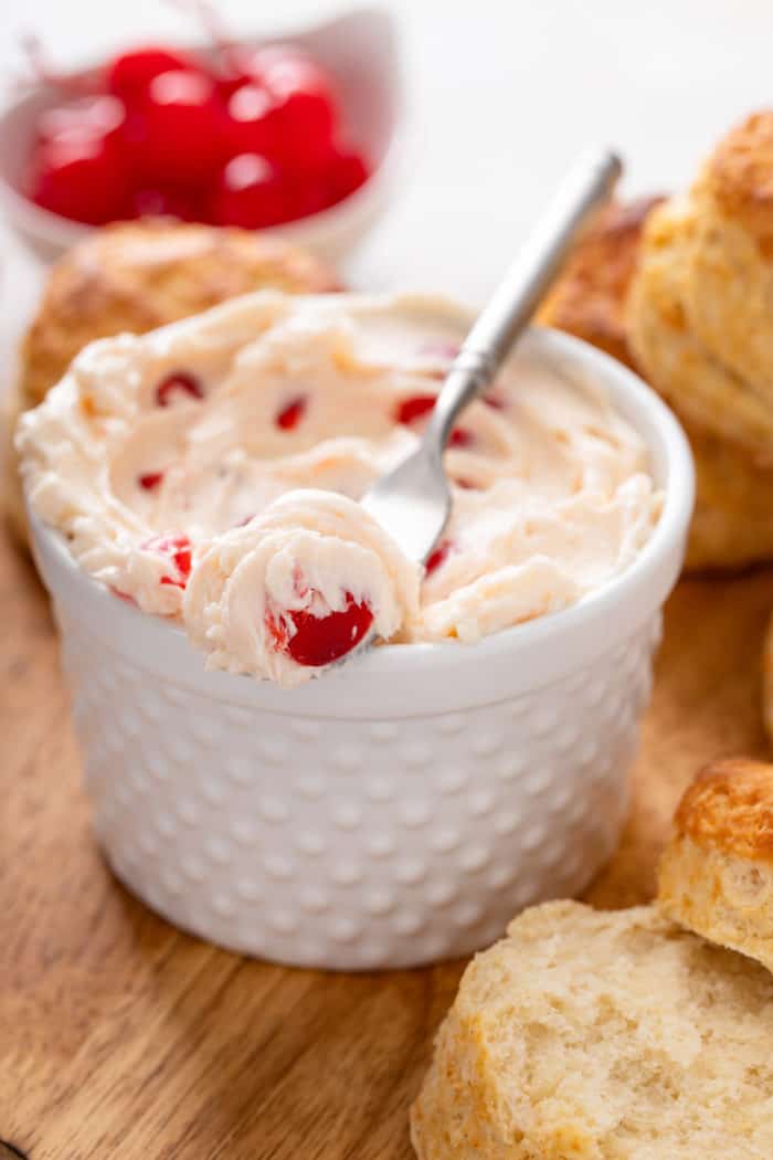 Knife with whipped cherry butter on it set across the top of a bowl of the butter.