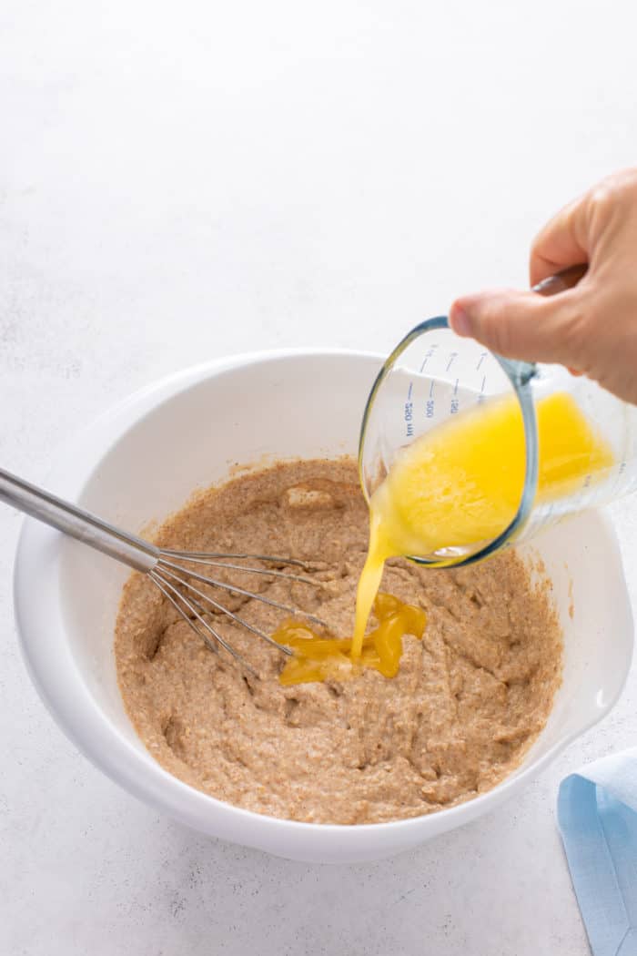 Melted butter being added to oatmeal pancake batter in a white mixing bowl.
