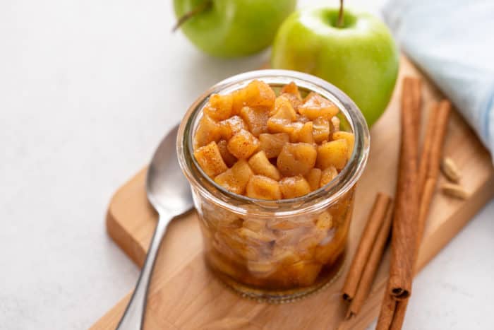 Jar filled with apple compote on a wooden board.