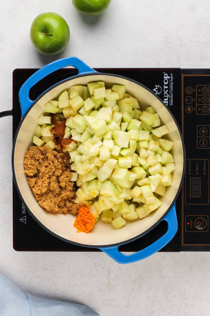 Ingredients for apple compote in a blue dutch oven on a burner.