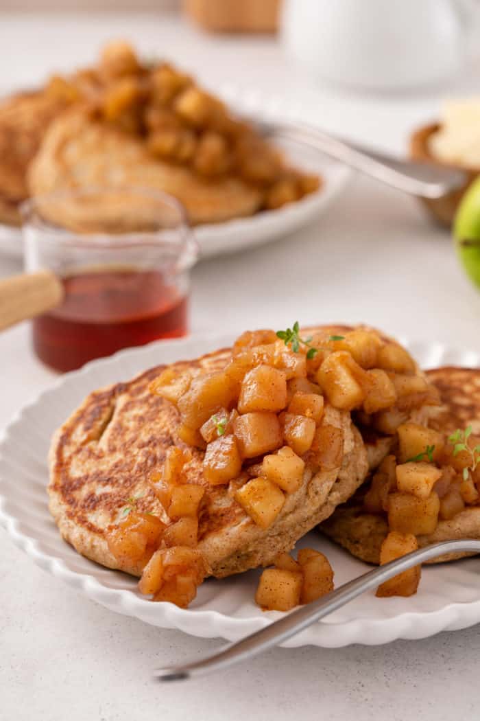 Apple compote over pancakes on a white plate.