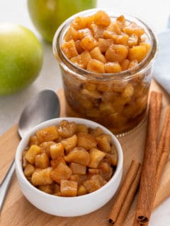 Two containers filled with apple compote on a wooden board.