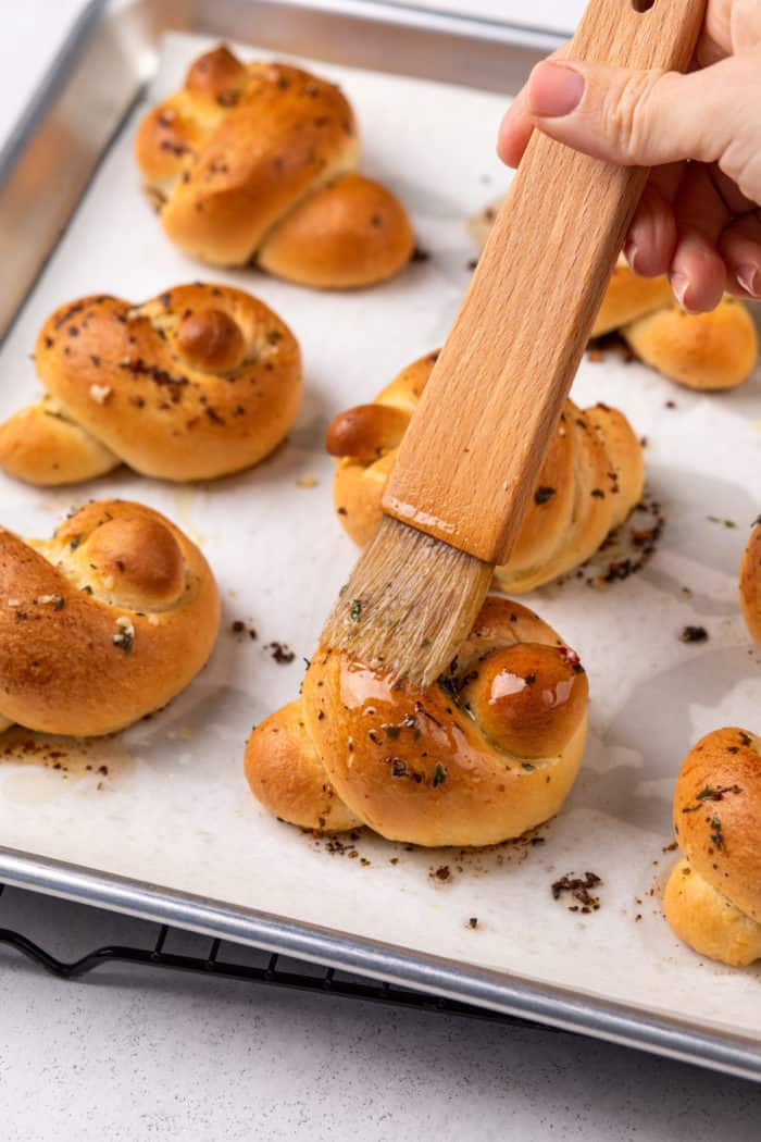 Garlic butter being brushed on top of baked garlic knots.