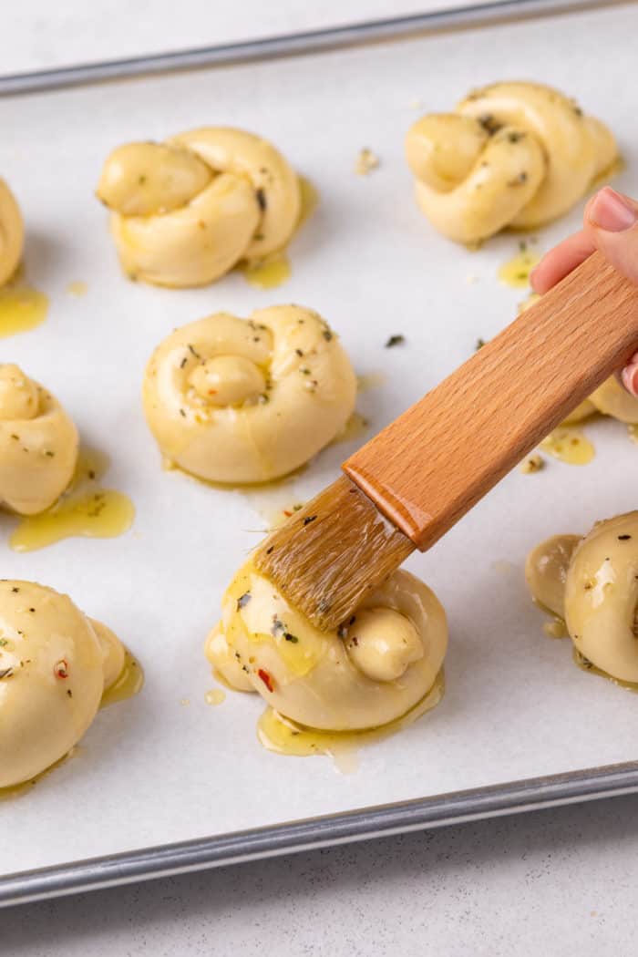 Garlic butter being brushed over unbaked garlic knots.