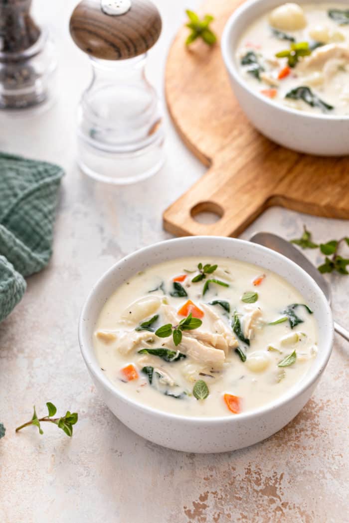 White bowl filled with chicken and gnocchi soup. A second bowl is set on a wooden board in the background.