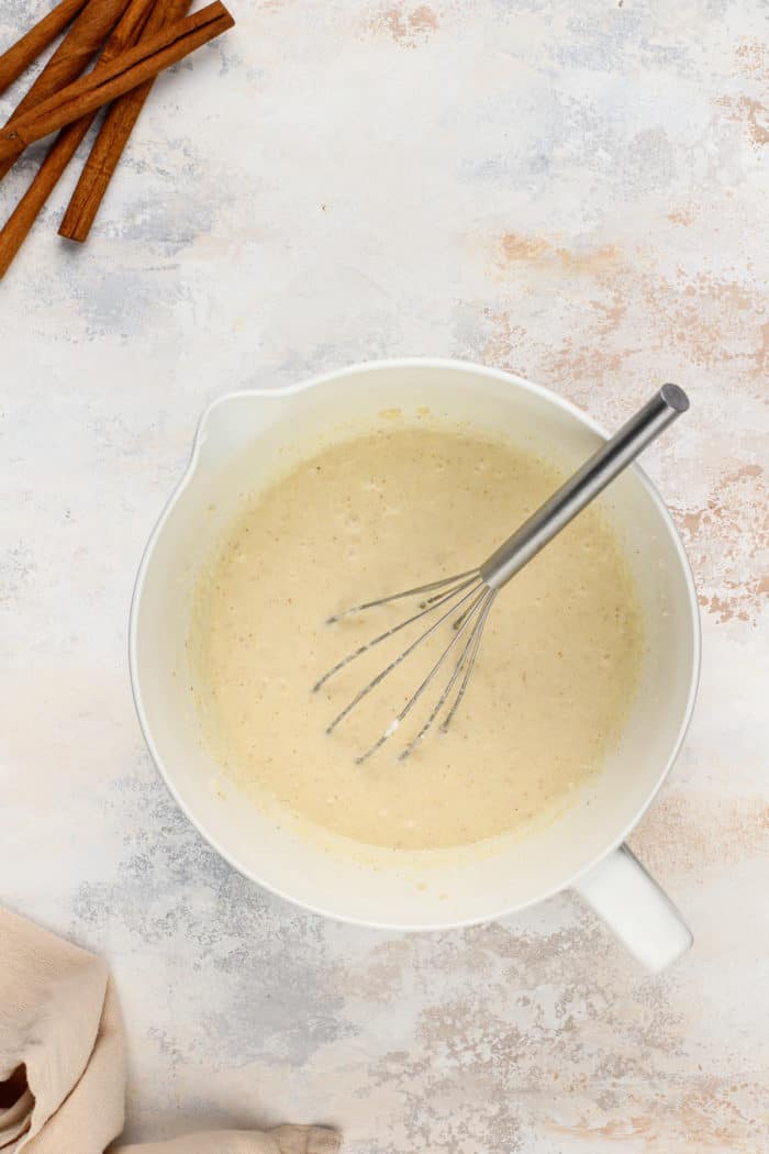 Wet ingredients for cinnamon roll cake whisked together in a white mixing bowl.