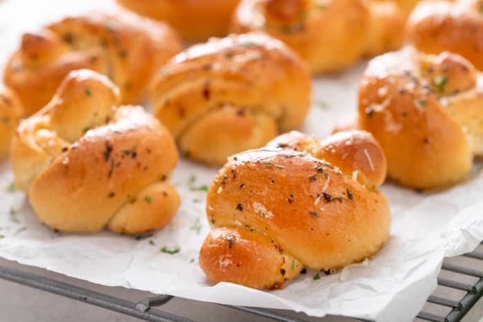 Baked garlic knots cooling on a wire rack covered in a piece of parchment paper.