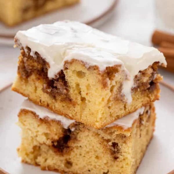 Two slices of glazed cinnamon roll cake stacked on a white plate.