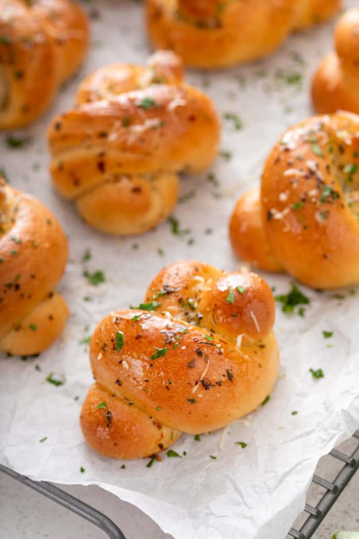 Close up of garlic knots arranged on a piece of parchment paper on top of a wire rack.