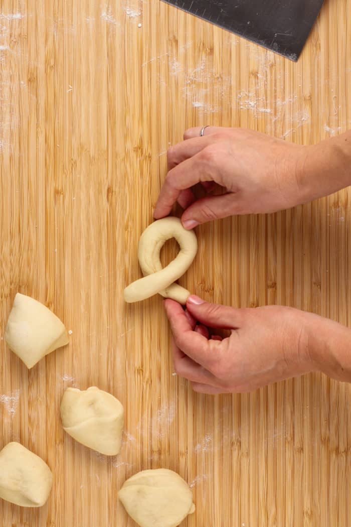 Hands shaping a snake of dough into a knot on a wooden board.