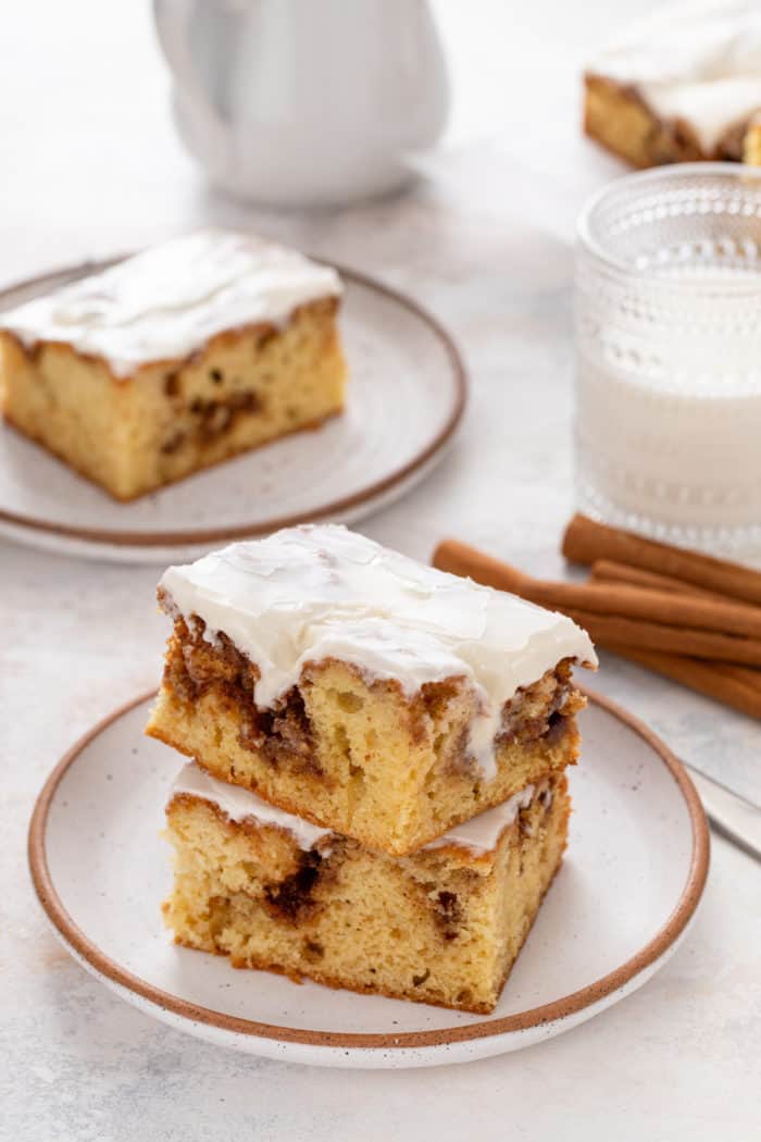 Two plates, each holding slices of cinnamon roll cake. A glass of milk is visible in the background.