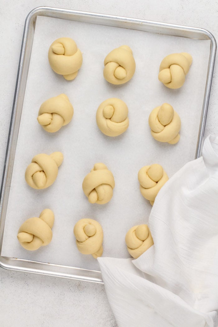 Risen garlic knots on a lined baking sheet, ready to go into the oven.