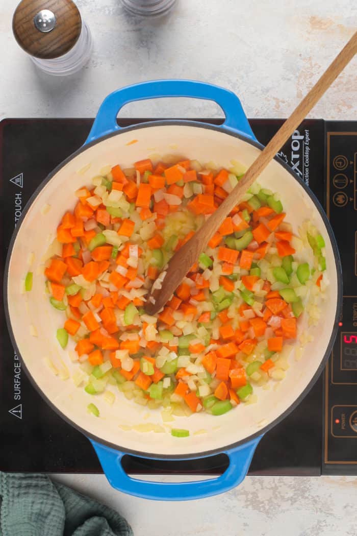 Cooked carrot, onion, and celery in a blue dutch oven.