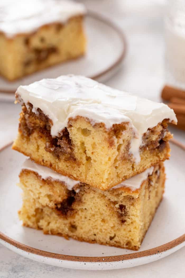 Two slices of glazed cinnamon roll cake stacked on a white plate.