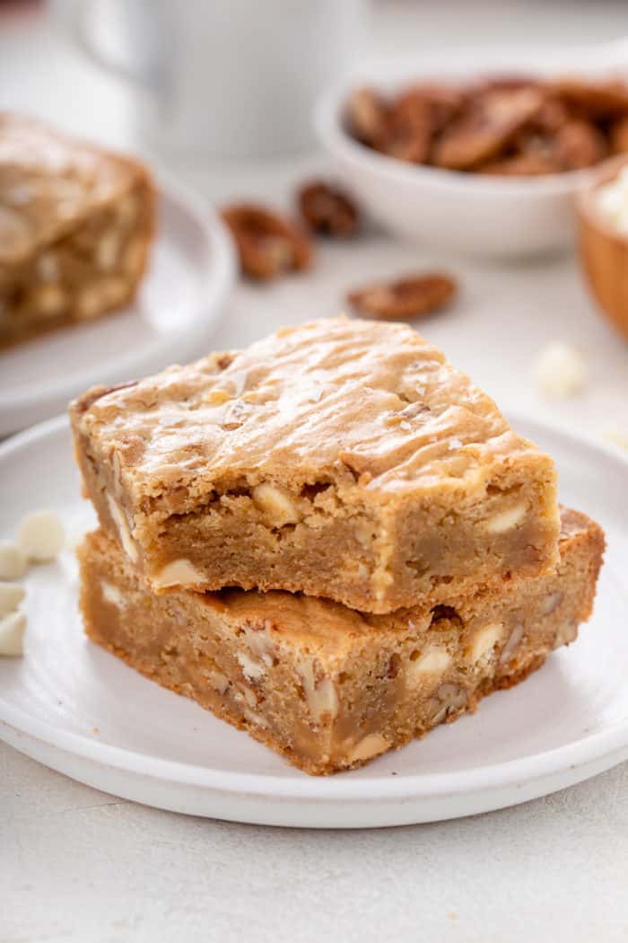 Two stacked white chocolate pecan blondies on a plate, with a bite taken from the corner of the top blondie.