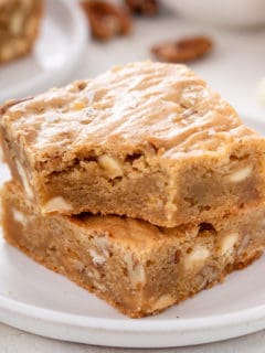 White plate with two white chocolate pecan blondies stacked on it.