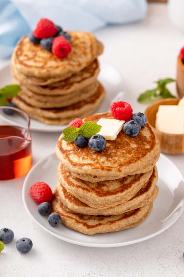 Two white plates, each holding a stack of oatmeal pancakes topped with fresh berries.