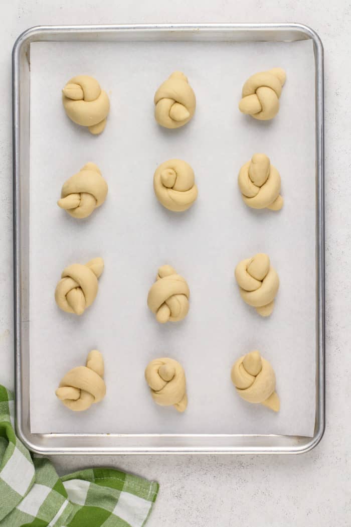 Shaped, unrisen garlic knots on a lined baking sheet.