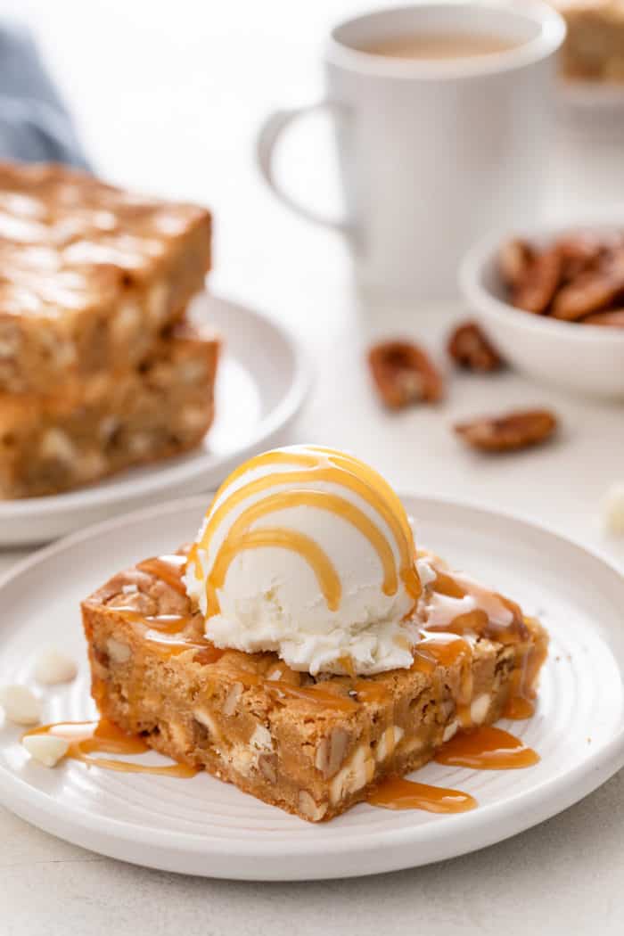 White chocolate pecan blondie topped with ice cream and caramel sauce on a white plate.