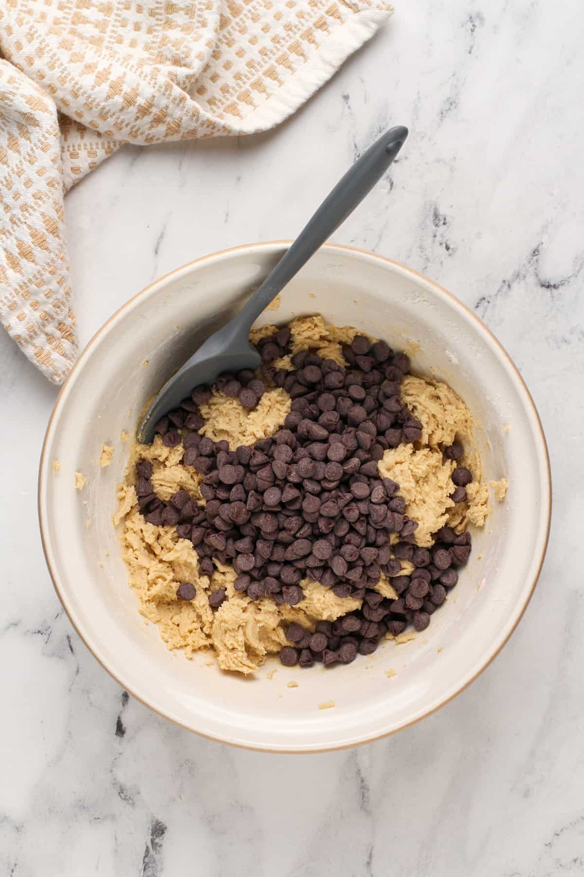 Chocolate chips being added to grand floridian chocolate chip cookie dough in a ceramic mixing bowl.