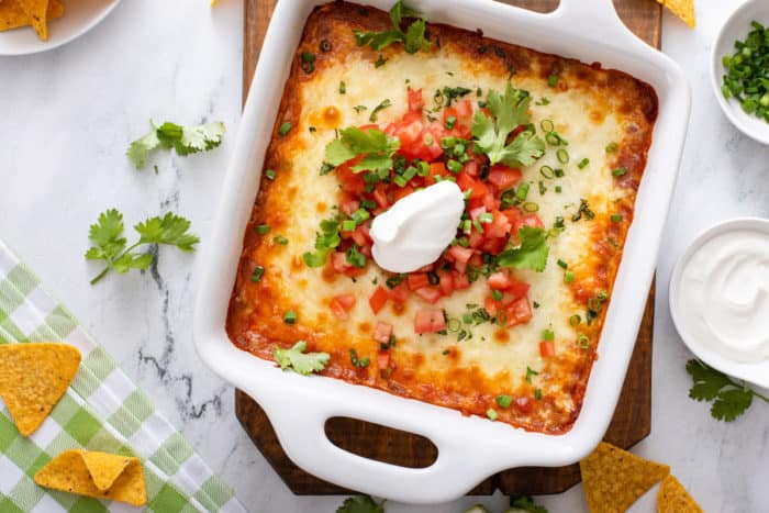 Overhead view of a white baking dish filled with chili cheese dip and garnished with cilantro, tomatoes, and sour cream.