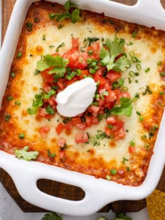 Baked chili cheese dip in a white baking dish, garnished with sour cream and tomatoes.