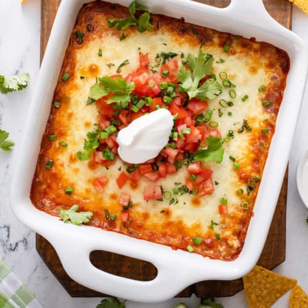 Baked chili cheese dip in a white baking dish, garnished with sour cream and tomatoes.