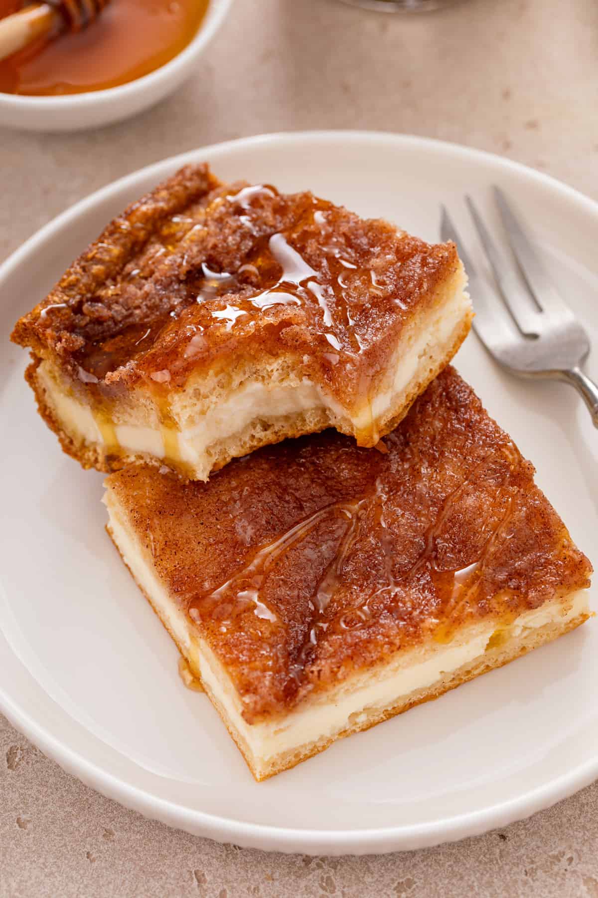 Two slices of sopapilla cheesecake on a white plate, with a bite taken from the corner from the top slice.