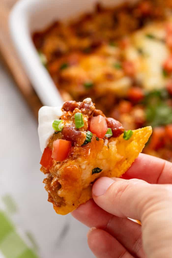 Hand holding up a tortilla chip loaded up with easy chili cheese dip.