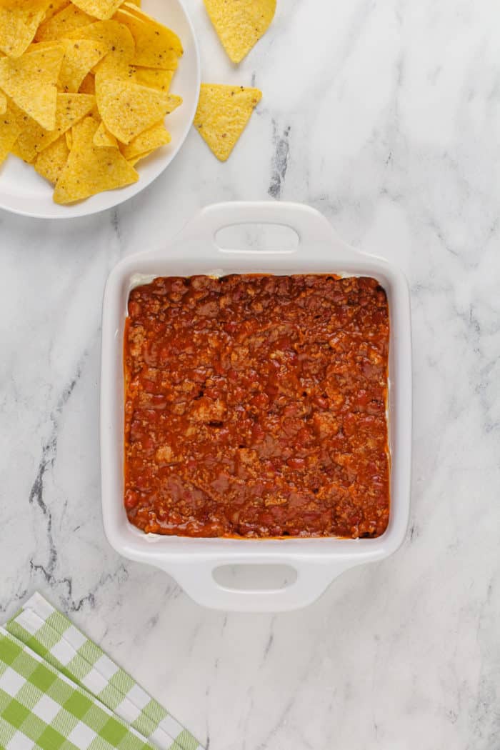 Chili layered on top of cream cheese in a white baking dish.
