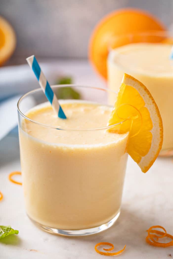 Close up of a glass of orange julius with a blue and white striped straw in it.