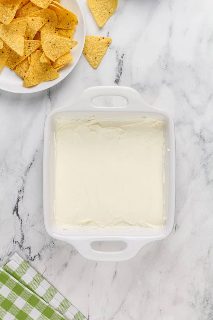Softened cream cheese spread in the bottom of a white baking dish.