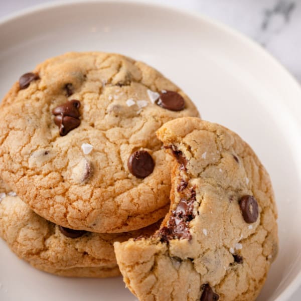 Three grand floridian chocolate chip cookies on a white plate. Two are stacked and the third has a bite taken from it and is leaning against the other two.