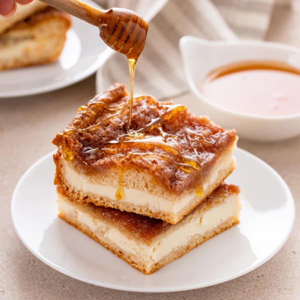 Honey being drizzled over two slices of sopapilla cheesecake.