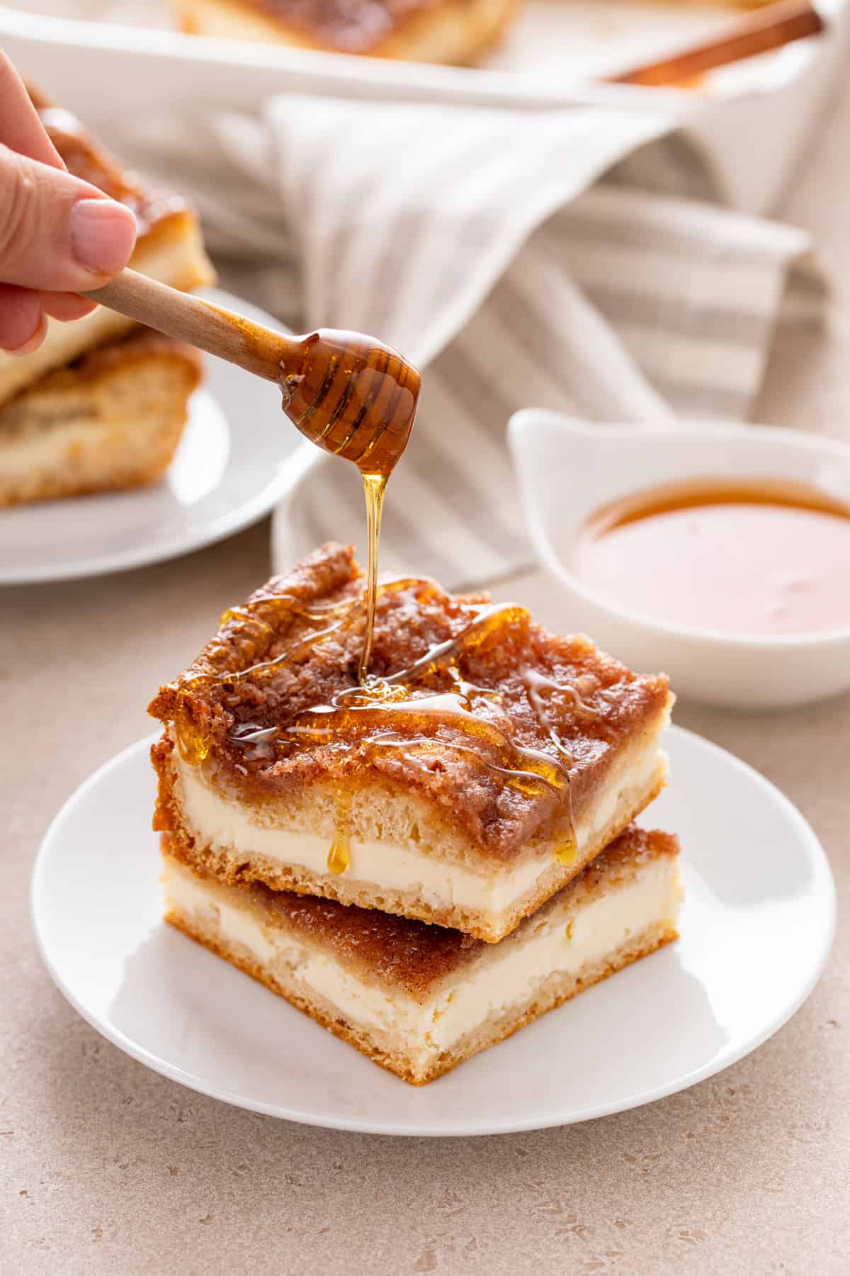 Honey being drizzled over the top of two stacked slices of sopapilla cheesecake on a white plate.