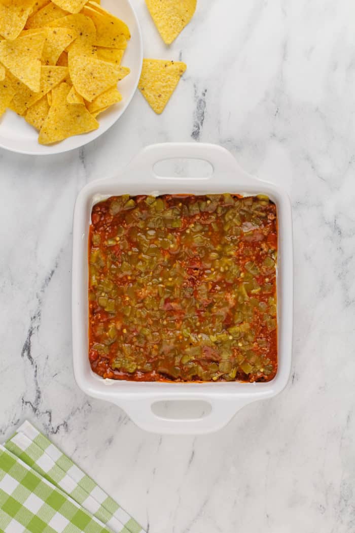 Diced green chilies layered on top of chili in a white baking dish.