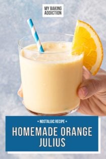 Hand holding up a glass of orange julius, garnished with a blue and white striped straw and an orange slice. Text overlay includes recipe name.