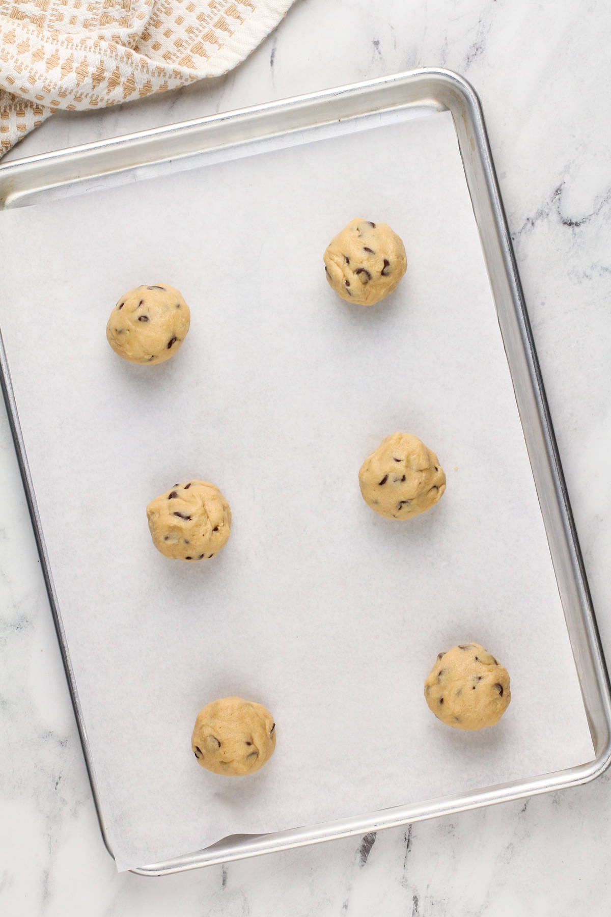 Six balls of grand floridian chocolate chip cookie dough on a parchment-lined baking sheet.