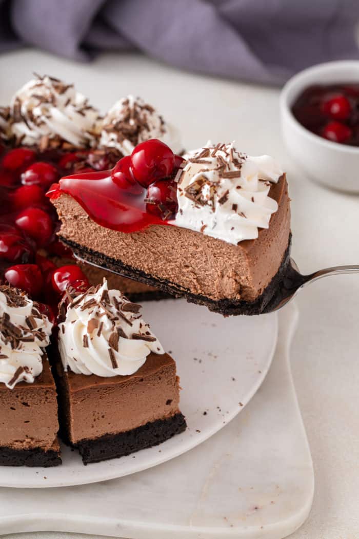 Cake server lifting a slice of black forest cheesecake from the cake plate.