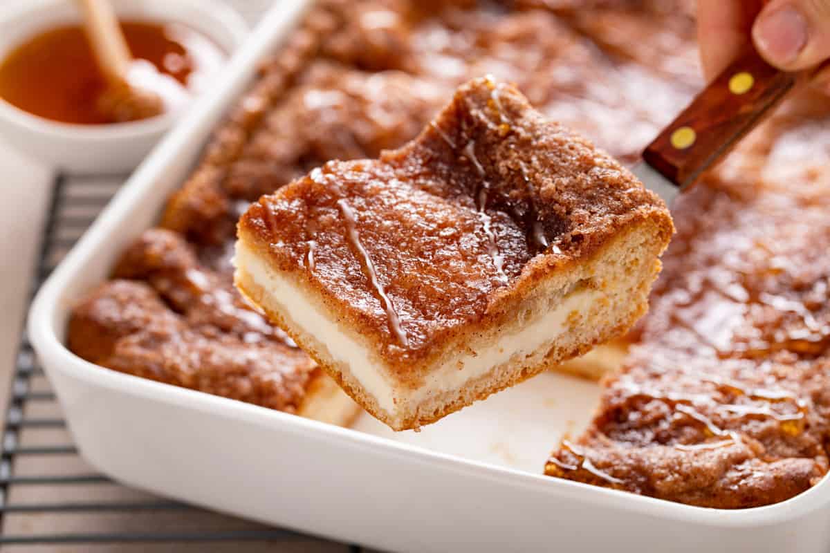 Cake server lifting up a slice of sopapilla cheesecake from a pan.