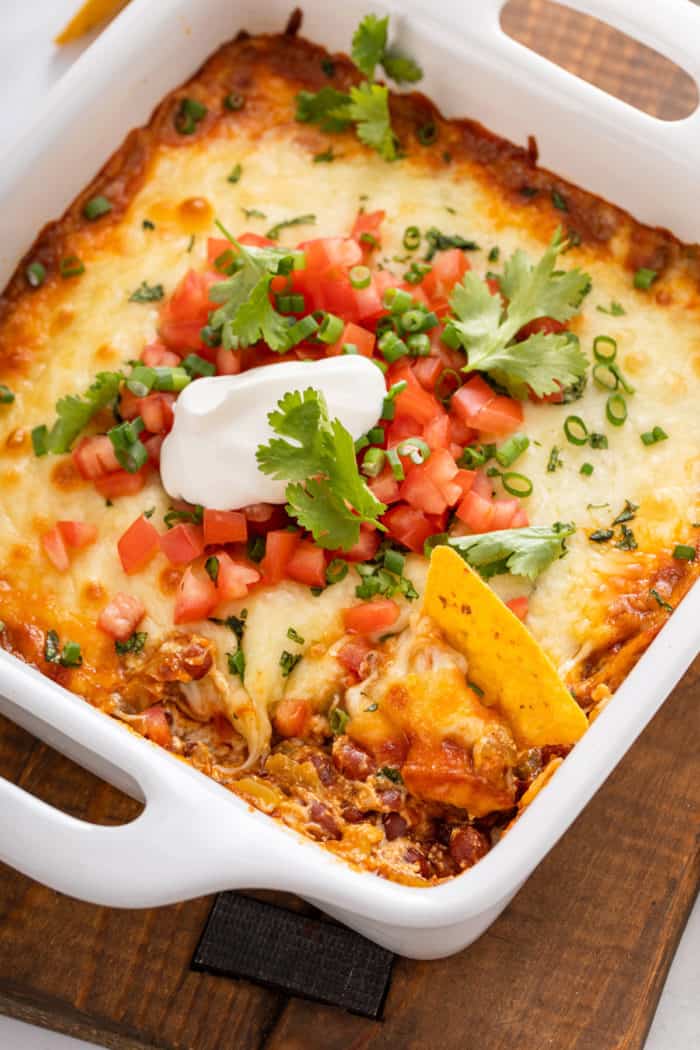 Baking dish of easy chili cheese dip with a tortilla chip in it.