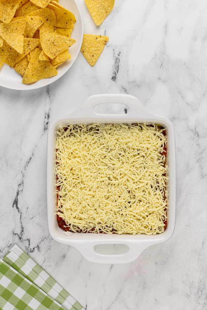 Chili cheese dip assembled in a white baking dish, ready to go in the oven.