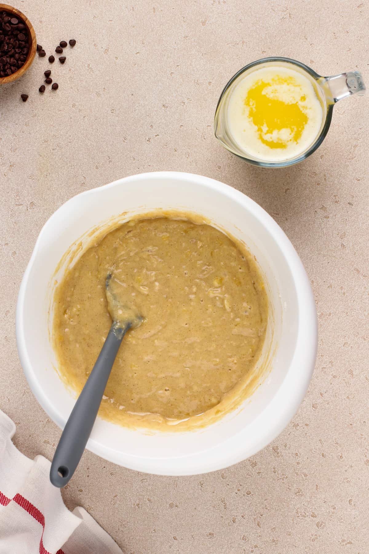 Batter base for banana bread in a white bowl next to a measuring cup of melted butter.