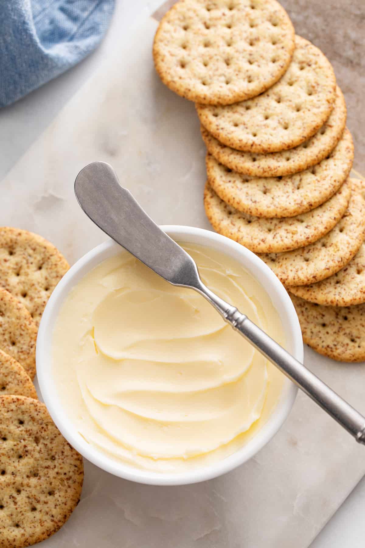 Bowl of butter surrounded by crackers on a marble board.