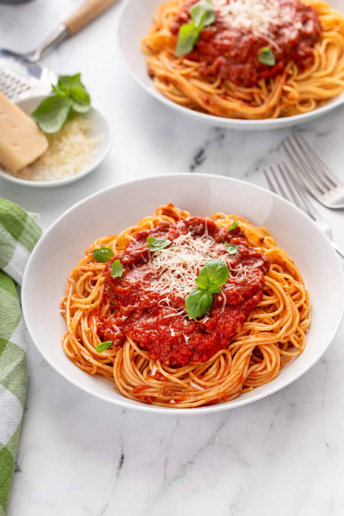 Two white bowls filled with spaghetti topped with sauce.