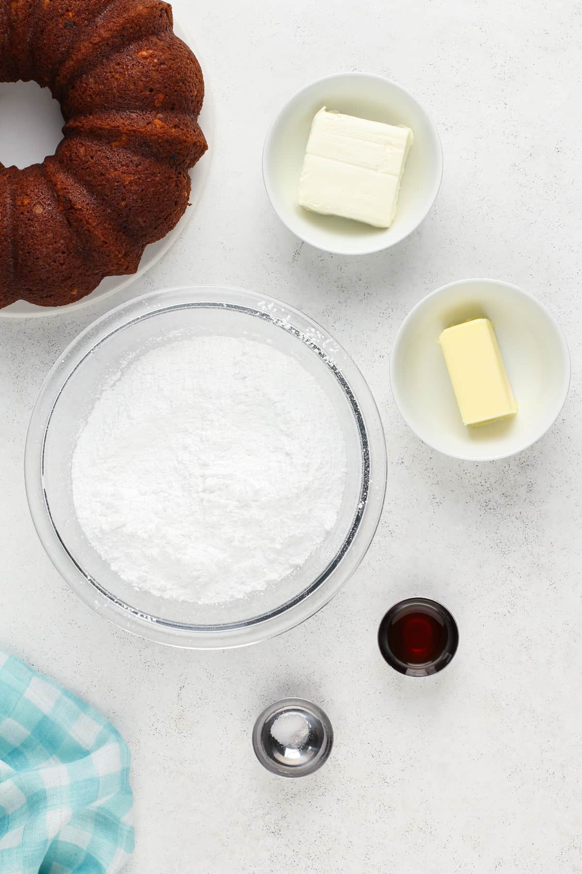 Ingredients for cream cheese frosting next to a bundt cake on a countertop.