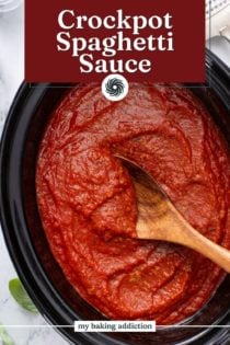 Wooden spoon stirring pureed spaghetti sauce in a slow cooker. Text overlay includes recipe name.