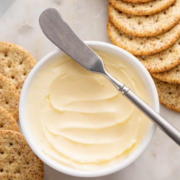 Bowl of butter surrounded by crackers on a marble board.