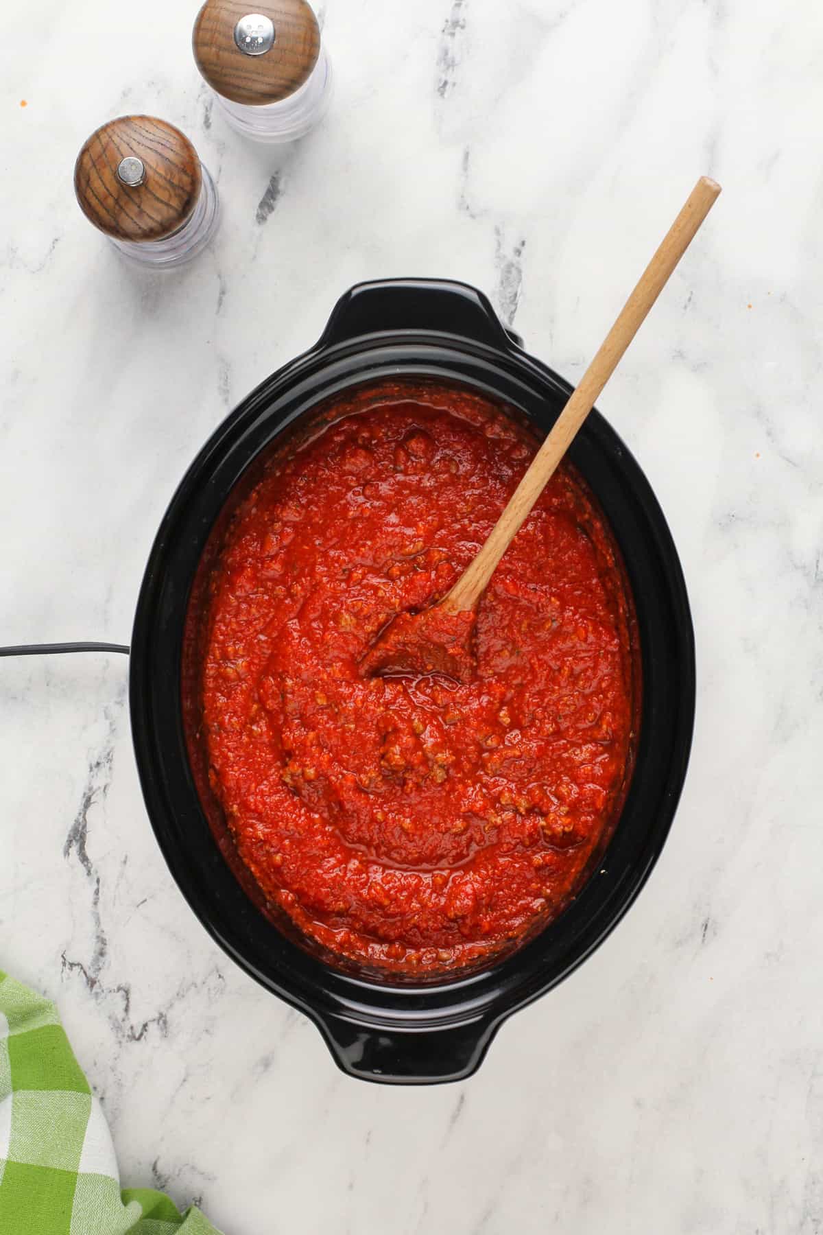 Wooden spoon stirring spaghetti sauce in a crockpot.