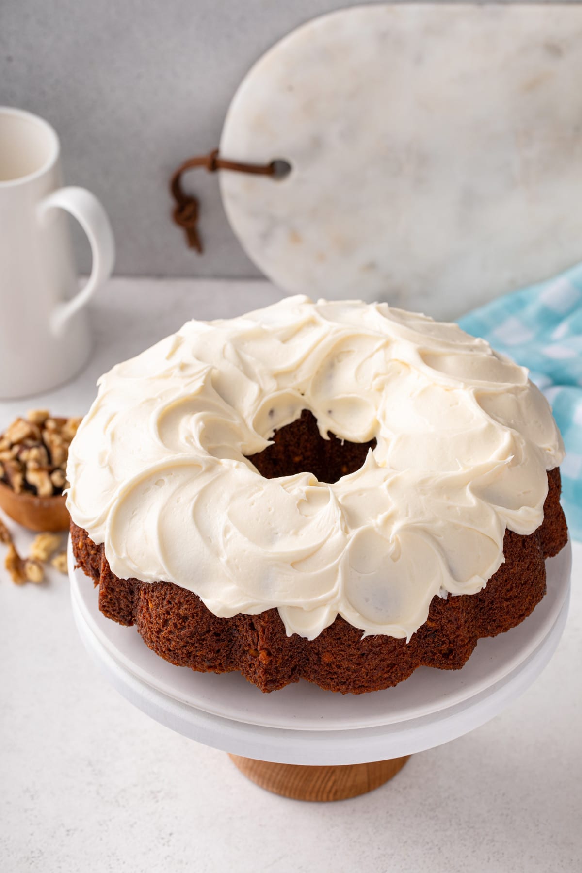 Carrot bundt cake frosted with cream cheese frosting on a white cake plate.